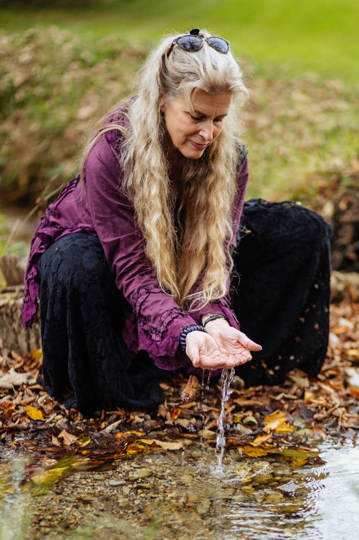 Die Künstlerin Anja Cantánima sitzt an einem fließenden Bach in der Natur